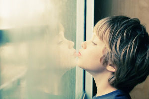 Photo of a boy looking sadly out a window to show loneliness of autism.