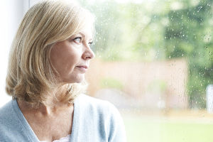 Photo of a middle-aged woman looking out a window looking melancholy.