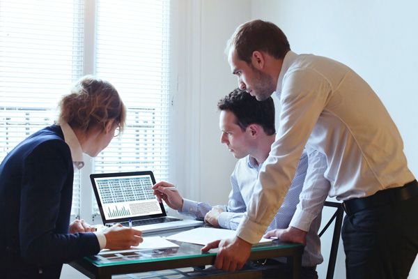 Photo of a team of business professionals around a computer engaged in problem solving.